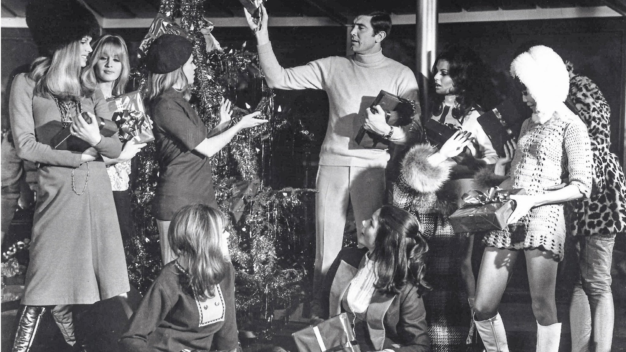 Black and white photo of a group of people gathered around a Christmas tree with presents.